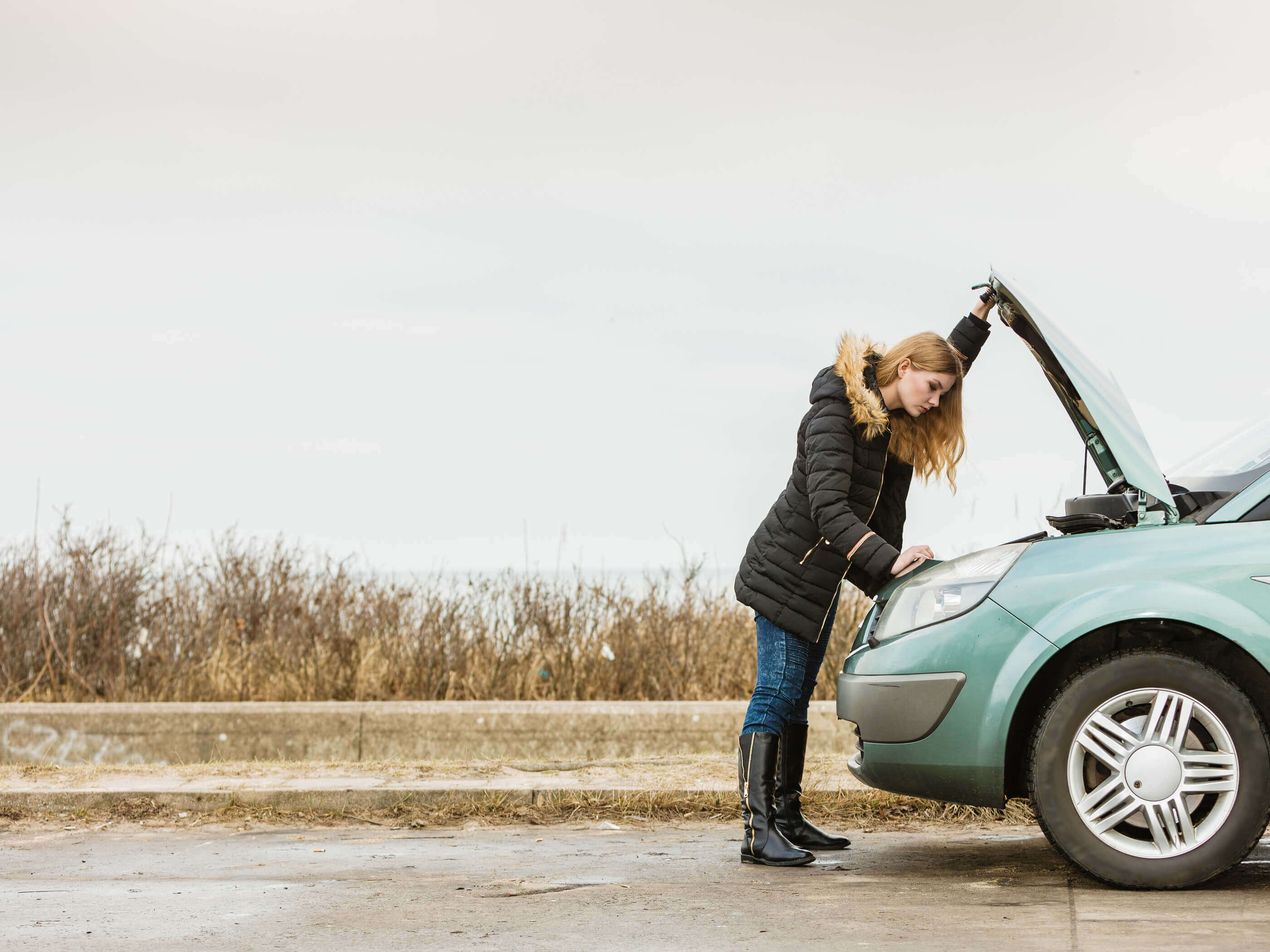 A woman looking under the bonnet of her broken-down car